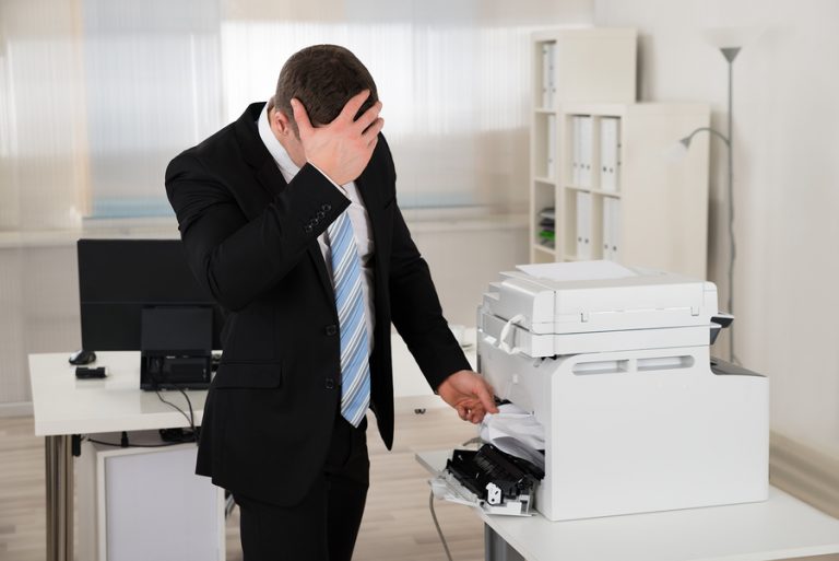 Irritated Businessman Looking At Paper Stuck In Printer